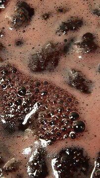 Dark bubbly liquid churns rapidly as wastewater contamination textures show frothy scum over murky sludge in industrial treatment vat closeup, with foam building over sediment and swirling surface