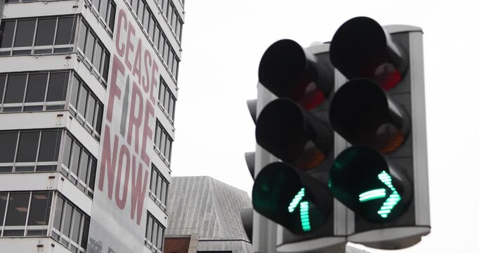Red traffic lights frame a &ldquo;CEASE FIRE NOW&rdquo; banner on urban building, symbolizing urgency of ending armed conflict, protecting civilians, demanding peace, calling for immediate humanitarian action.