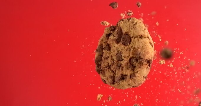 Chocolate chip cookie falling with crunchy crumbs on red background in slow motion