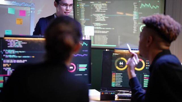 Smiling Asian team lead in a suit shows a sticky note at the code screen as a thoughtful Black engineer rests a stylus on his chin beside a Latina colleague seen from behind