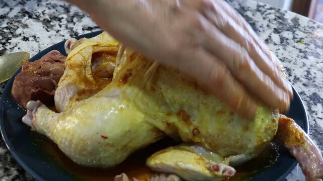 Hands spreading marinade under the skin of a whole raw chicken