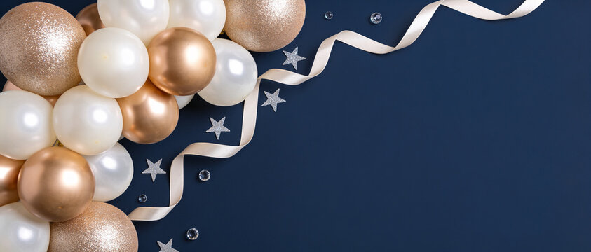 A cluster of metallic gold and white spheres with curly ribbons and stars on a dark navy background with copy space