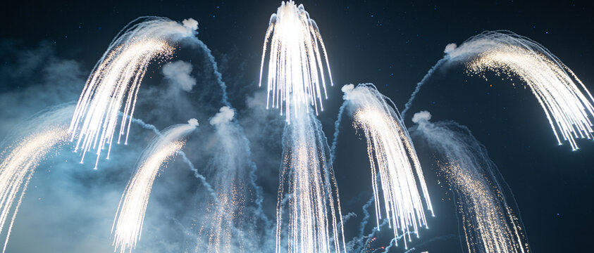 White fireworks trails exploding against a dark night sky with smoke