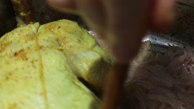 Cooking a whole marinated chicken with onions in a steel pot