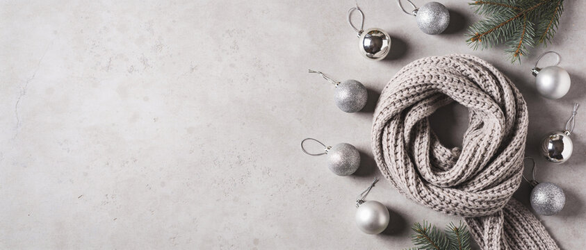 Coiled beige knitted yarn with silver Christmas baubles and fir branches on a white concrete background with copy space
