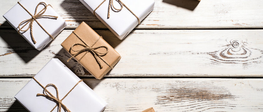 White and brown gift boxes with twine bows on a rustic wooden table.