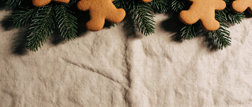Gingerbread cookies arranged on green fir branches at top of white fabric