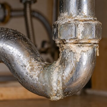 Close-up of corroded metal pipe joint coated in heavy mineral scale. Limescale buildup and rust in worn plumbing. Hard water damage and pipe maintenance. Household plumbing deterioration.