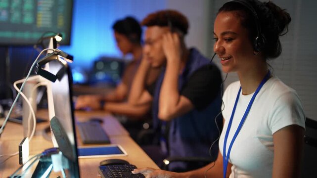Latina operator with a headset closes her eyes as she speaks, then smiles and works the mouse as a Black colleague rubs his head and an Asian teammate types in the background.