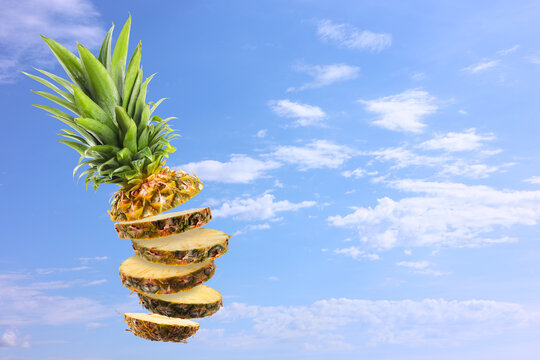 Sliced fresh pineapple in air against blue sky with clouds