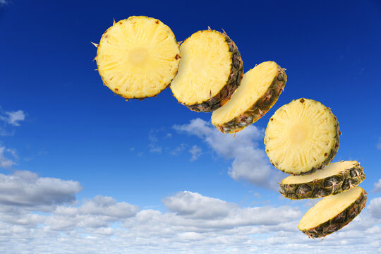 Pineapple slices in air against blue sky with clouds