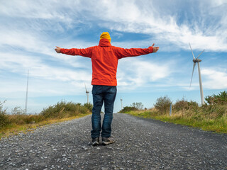 Person stands with arms wide open on gravel road. Red jacket and yellow hat contrast with blue sky. Feels freedom, peace, or adventure. Great for travel, wellness, or outdoor lifestyle themes. © mark_gusev