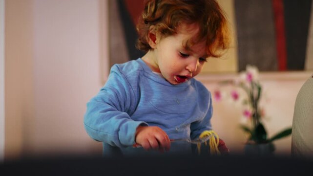 Little Caucasian boy slurping spaghetti noodles with his hands at home