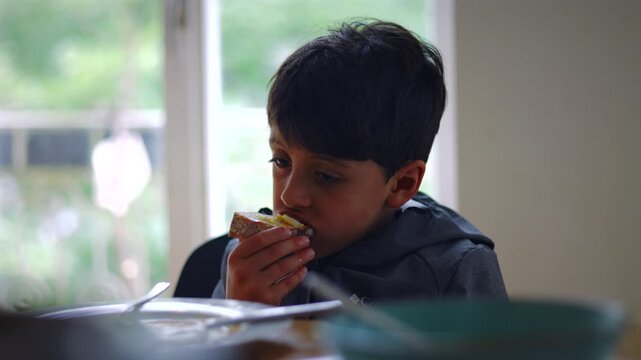 Caucasian boy biting into a slice of toast at the breakfast table