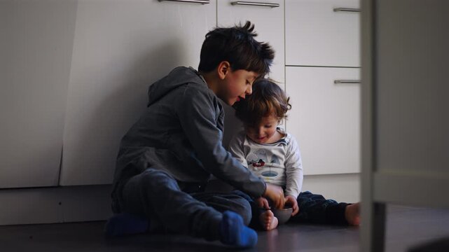 Caucasian big brother sharing his snack with toddler sibling