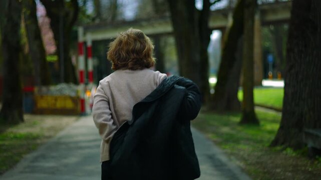 Older Caucasian woman putting on her jacket while walking away