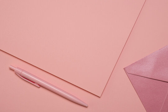 Blank pink paper partially visible beside a pen and glitter envelope on a pale pink background, top view with copy space