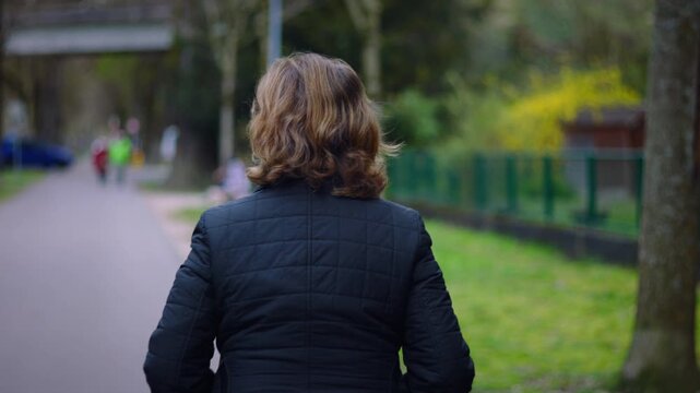 Elderly Caucasian woman walking away along a park path on a spring day