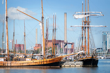 Historic sailing ships with tall masts moored in a harbor, with calm blue water and a modern city skyline in the background. Traditional vessels and maritime heritage in an urban waterfront setting. © Svitlana