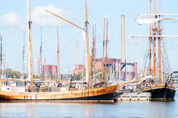 Historic sailing ships with tall masts moored in a harbor, with calm blue water and a modern city skyline in the background. Traditional vessels and maritime heritage in an urban waterfront setting. © Svitlana
