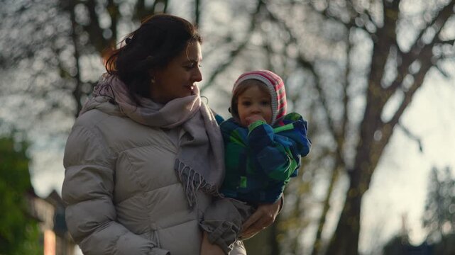 Caucasian mother holding her baby outdoors in winter under bare trees