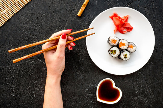 Hand takes sushi roll with salmon and avocado with chopstick. Black background top view