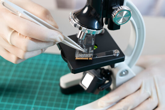 Close up of engineering specialist inspecting microchip components on server storage module under microscope