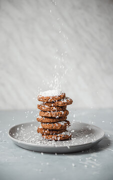 Coconut flakes falling onto a stack of homemade cookies on a plate