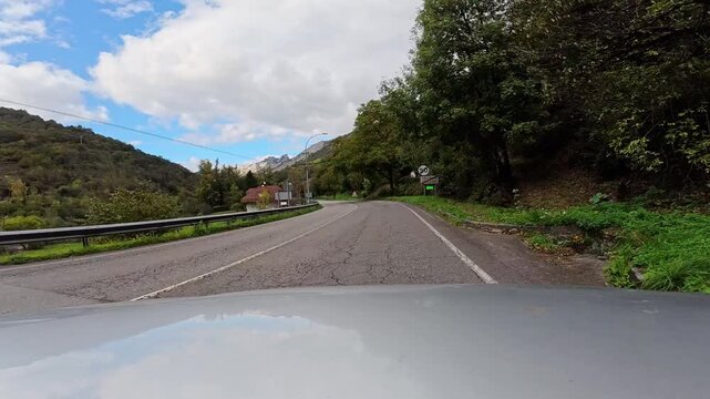 Vehicle driving along a winding asphalt road through green mountains and small villages in asturias, spain