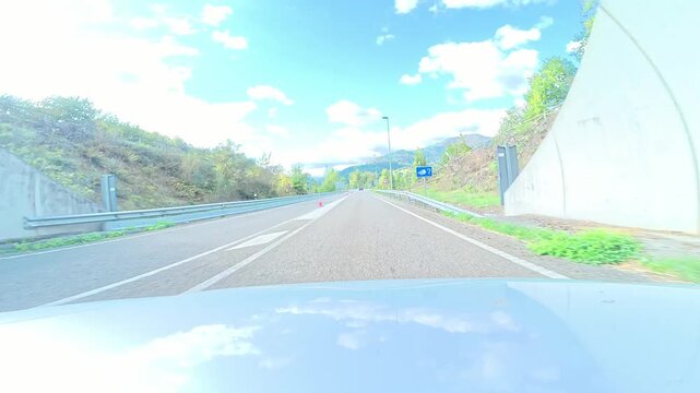 Car hood view driving fast along a scenic highway and passing through a tunnel in aller valley, spain, on a sunny day
