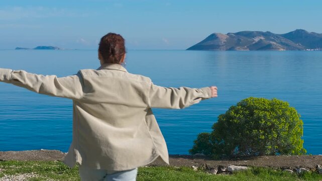 Tourist enjoying freedom with open arms in front of the sea. Youthful traveler standing with outstretched arms, experiencing profound sense of freedom against scenic mediterranean seascape