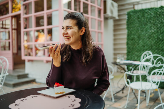 Woman smiling while recording a voice message at an outdoor cafe