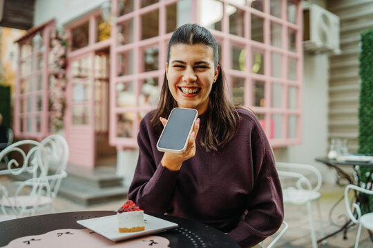 Smiling woman holding a smartphone at an outdoor cafe with dessert
