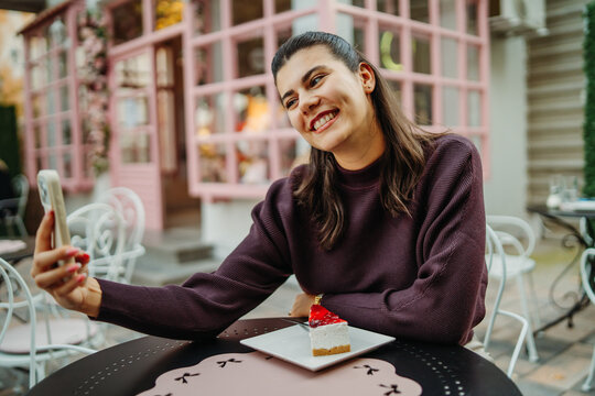 Woman taking a selfie with cake at an outdoor cafe