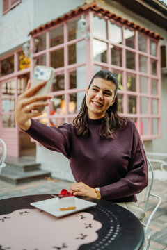 Woman taking a selfie at a cafe with cake on the table