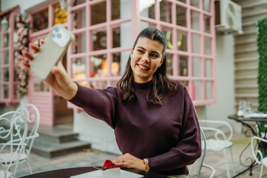 Woman taking a smartphone selfie at a pink caf&eacute; patio