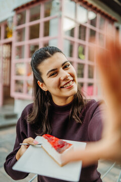 Smiling woman holding cheesecake at an outdoor cafe