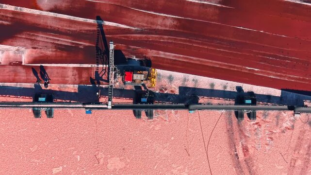 Top down view of mechanical salt harvester on red field. Heavy industrial equipment leaves dark tracks on pink crystallized surface during extraction.