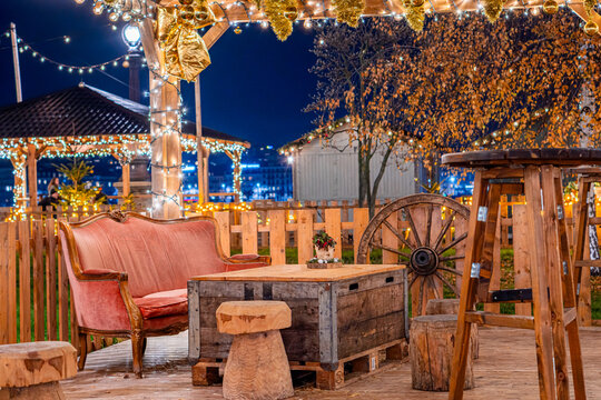 View of a cozy outdoor seating area with a vintage pink sofa, rustic wooden table, and festive string lights at the Christmas market in Montreux, Vaud, Switzerland.
