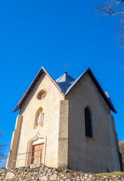 View of the historic chapel in Montvernier featuring stone walls, a statue in a niche, and a cross on the roof under a clear blue sky in Montvernier, Auvergne-Rhone-Alpes, France.