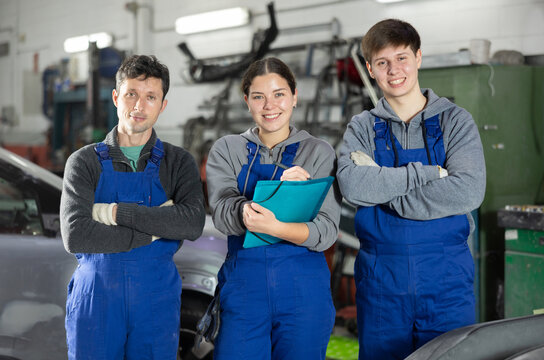 Team of positive auto mechanics, two men and one woman, wearing blue overalls and posing, ready to provide professional vehicle service