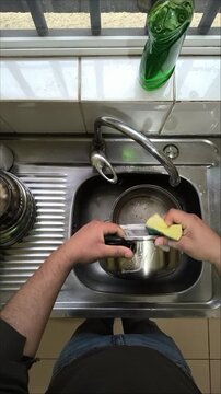 Vertical top-down stock footage of person washing stainless steel pot in kitchen sink