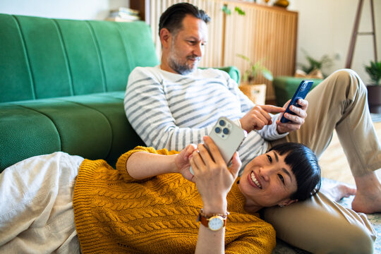 Woman resting on partner's lap while using smartphones at home
