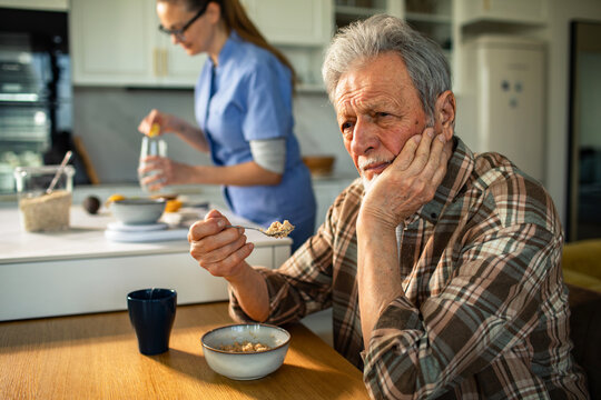 Senior man hesitant to eat breakfast as caregiver prepares food