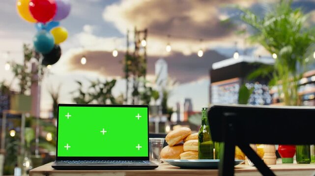 Laptop with editable green screen beside drinks at rooftop party
