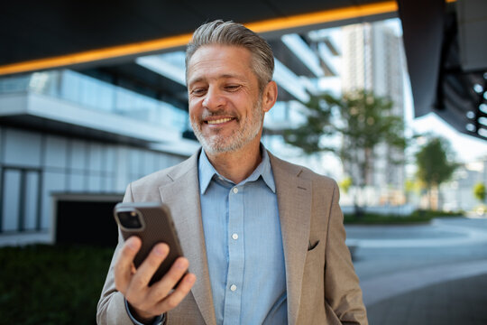 Smiling businessman checking smartphone outside modern office building