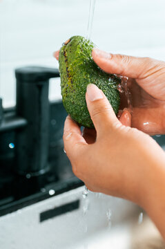 Hands washing fresh avocado under running water