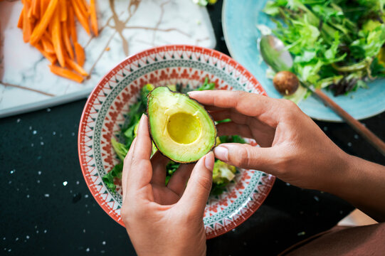Hands holding avocado halves preparing vegetarian salad meal