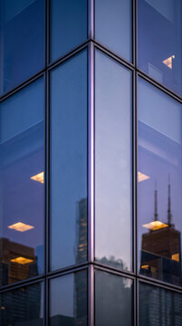 Reflective glass facade corner detail mirroring distant towers in precise corporate architecture