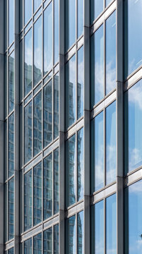 Geometric glass curtain wall of corporate skyscraper reflecting clouds in vertical composition